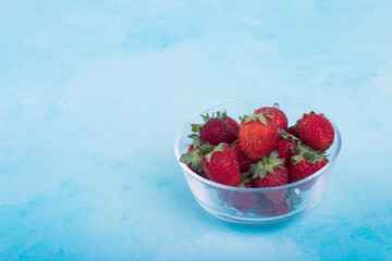 Red strawberries in a glass cup on blue background, top view