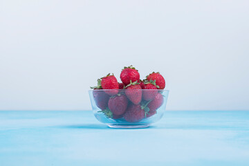 Red strawberries in a glass cup on blue background in the center
