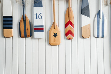 Several colorful wooden paddles hang on a white wall or fence. canoe paddles for active water sports decorative.