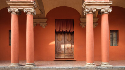 Red arcade with columns and a door, famous Portico Of Bologna in Italy.
