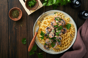 Fusilli pasta with mushrooms, cheese and garlic creamy sauce on plate on old wooden dark table background. Top view. Traditional Italian cuisine.