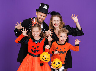 Cheerful family   in carnival costumes does scary gesture and celebrate Halloween on  colored purple background