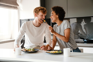 Young multinational couple smiling while having breakfast at home
