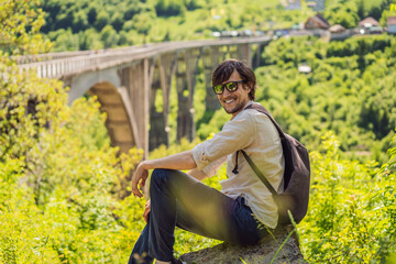 Montenegro. Man tourist in background of Dzhurdzhevich Bridge Over The River Tara. Travel around...