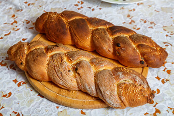 Fried challah with sesame seeds on a wooden round board on a white tablecloth.