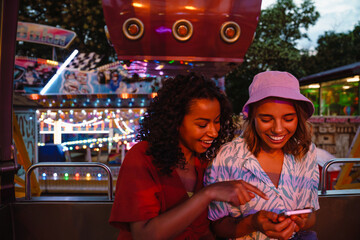 Young multiracial women using cellphone while riding on ferris wheel