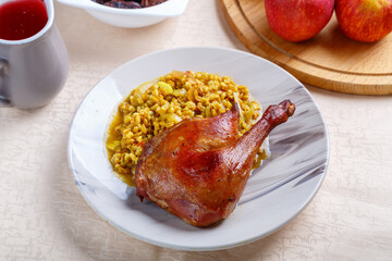 Amber boiled spelt with duck leg baked in a plate on a white tablecloth next to fragments of other food.