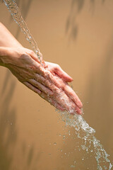 Fototapeta premium Close up of a female wet hands with water gliding over it on a beige background,