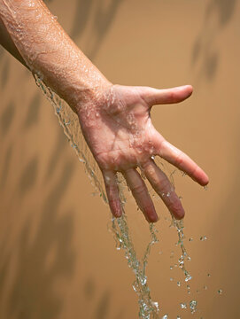 Close up of a female wet hand with water gliding over it on a beige background,