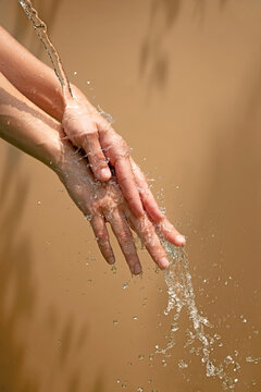 Close up of a female wet hands with water gliding over it on a beige background,