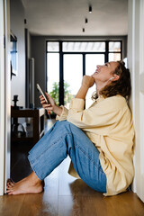 Fototapeta na wymiar White woman using cellphone with earphones sitting on floor at home