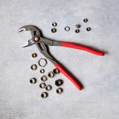 Adjustable pliers with insulated handles and fastening nuts lie on a concrete background