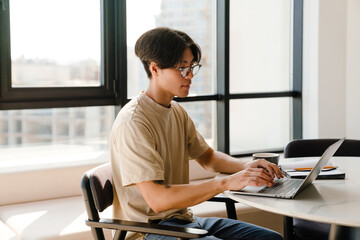 Asian young man studying with laptop while sitting by table at home