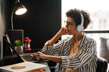 Fototapeta na wymiar Young black woman in headphones working with laptop