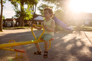 boy of caucasian appearance with curly hair riding on a seesaw in the park