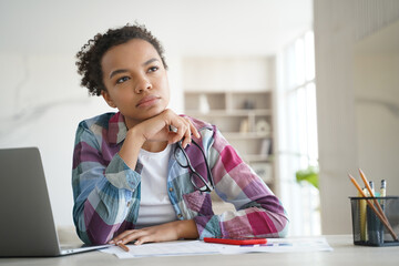 Pensive mixed race teen girl school student looks aside lost in thoughts while learning at home