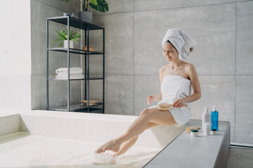 Young woman massaging hips to prevent cellulite sitting on bathtub. Body care, spa procedure