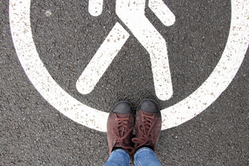 Fototapeta premium The pedestrian sign is drawn on the pavement and next to it are female legs in sneakers, a pedestrian road