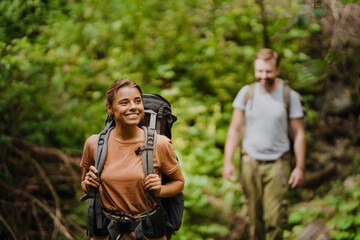 White young couple with backpacks hiking in green forest