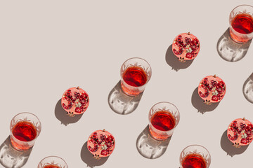 Creative pattern made of a half of pomegranate and glass with juice or red wine on pastel beige background. Summer fruit and refreshment  concept. Minimal style. Sunlit flat lay. Top view