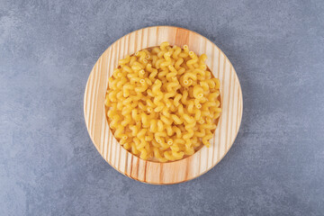 Raw dry macaroni on wooden plate
