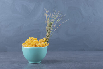 Raw dry macaroni in blue bowl with wheat