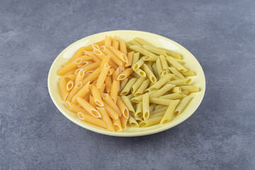 Raw green and yellow penne pasta on yellow plate
