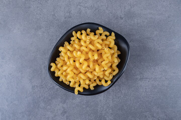Raw dry macaroni in black bowl