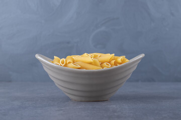 Raw penne pasta in ceramic bowl