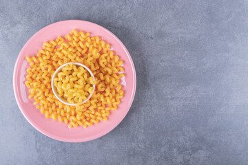Raw dry macaroni on pink plate
