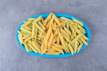 Raw green and yellow penne pasta on blue plate