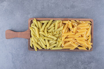 Raw green and yellow penne pasta on wooden board