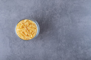 Raw pasta in glass on stone background