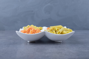Raw penne and heart-shaped pasta on white plate