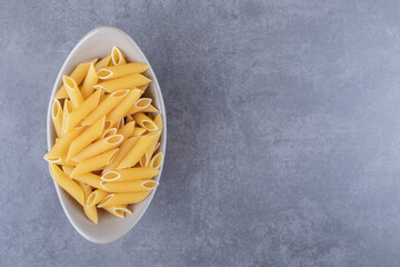 Raw penne pasta in ceramic bowl