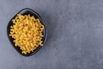 Raw dry macaroni in black bowl