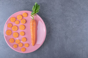 Whole carrots with sliced carrots on a plate, on the marble background