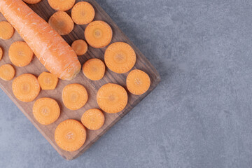 A wooden board of sliced and whole carrots , on the marble background