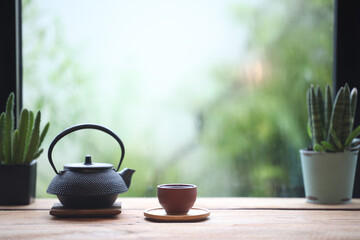 tea cup and metal pot on wooden table in front of window