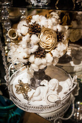 Winter decorative Christmas bouquet of cotton wool, cones, artificial flowers, ribbons and decorations, on an iron tray with a ceramic angel.