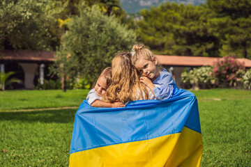 Ukrainian mother with two children with flag of Ukraine. Outside. Concept of problem of war in Europe, supporting of families and children, migrants, emigration, patriotism, motherhood, Ukrainian