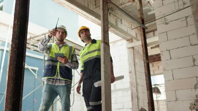 Two professional male civil engineer or Architect, inspector with contractor, foreman or worker. While look at blueprint plan inspect discuss meeting building project on construction site.