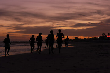 Fototapeta premium Silhouette of young fitness boys model of a soccer beach team jogging, running at sunrise sea in Rome Italy in a romantic sunset