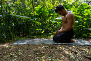 Young latin man arranging his yoga mat, inside a forest on a plain, direct contact with nature, mexico