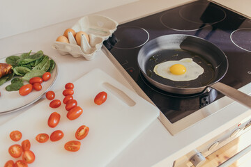 Egg on frying pan near cherry tomatoes and spinach in kitchen.
