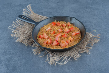 Fried pasta with tomato slices on black pan