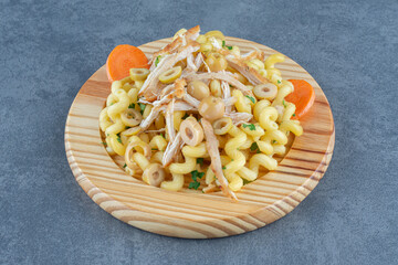 Delicious pasta with chopped chicken on wooden plate