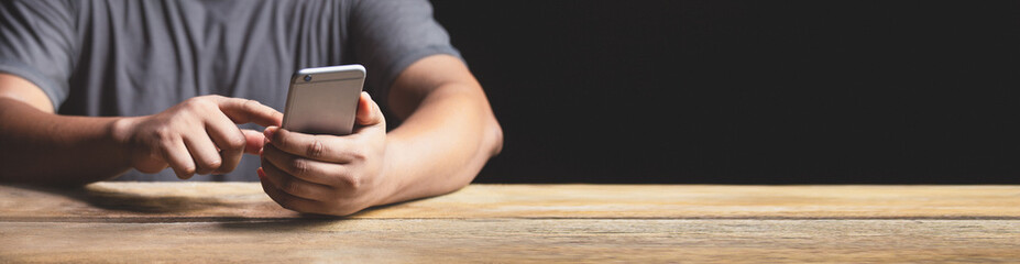 Hand using mobile phone or smartphone on wooden table. Technology background for web banner.