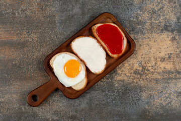 Toast with fried egg, cream cheese and jam on wooden board