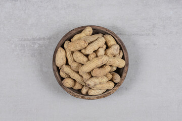 Wooden bowl of shelled peanuts on marble background